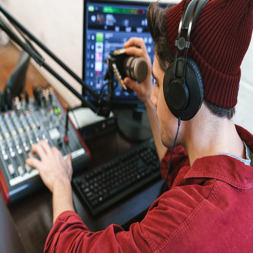 Image of young happy caucasian dj man wearing headphones working at radio station while making podcast recording for online show